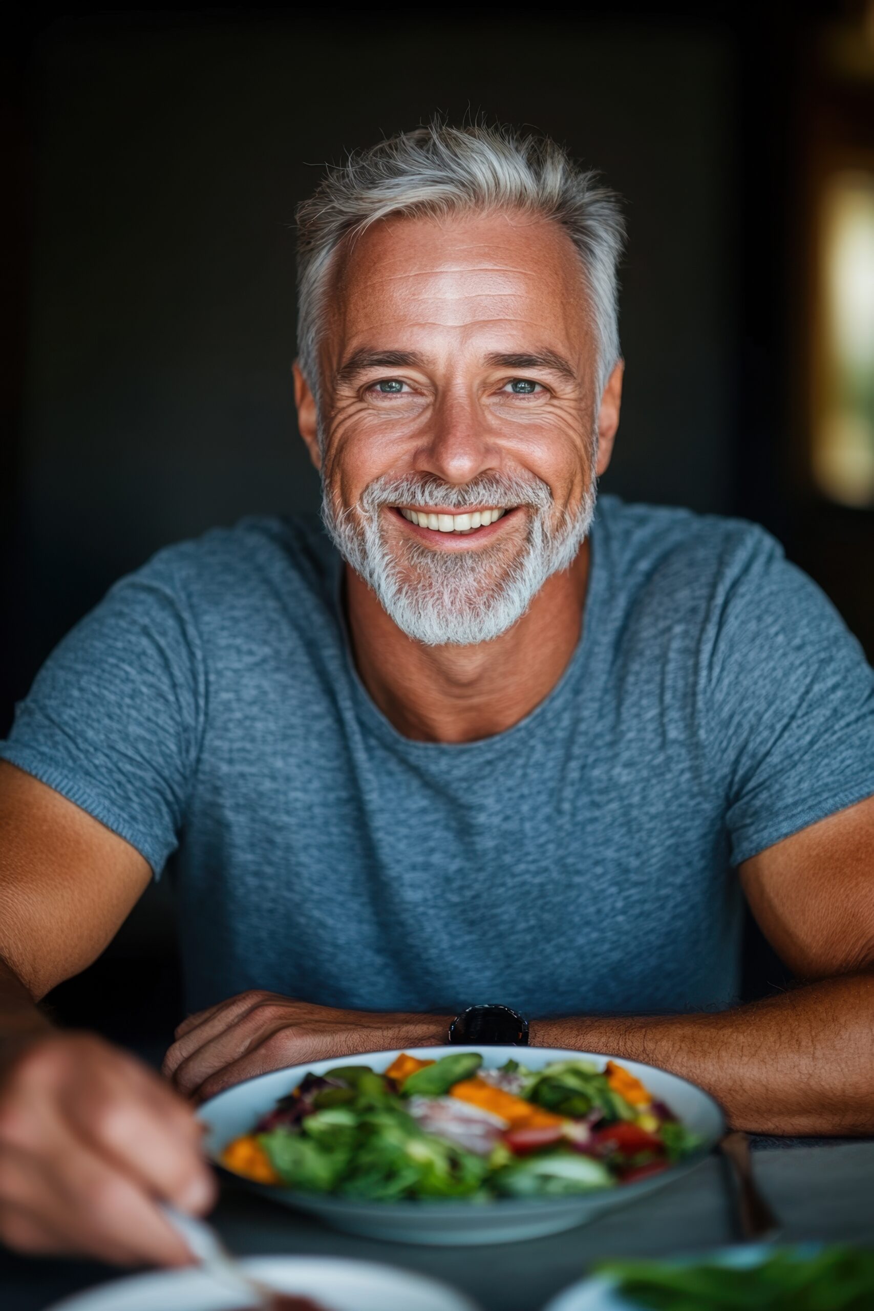 A healthy older man smiles while eating a plate of vegetables